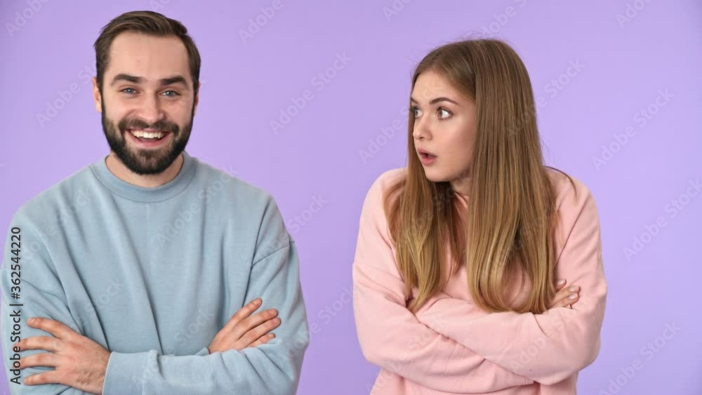 Displeased blonde woman standing with crossed arms and offended by her boyfriend which having fun over purple background Displeased blonde woman standing with crossed arms and offended by her boyfriend which having fun over purple background