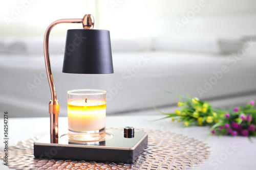 The luxury lighting aromatic scent  glass candle is put on the electric lamp candle warmer heater on the grey table in the white bedroom to create relax and romantic ambient