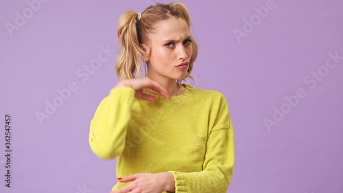 A beautiful blonde girl maliciously twists hair on her finger and looks at the camera on a purple background in an isolated studio photo