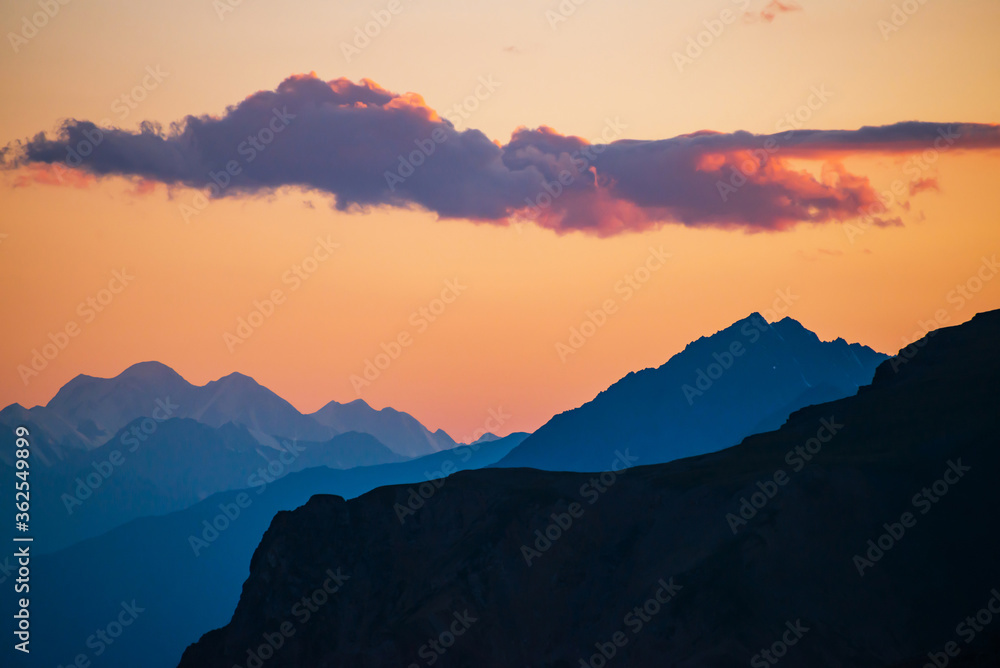 Colorful dawn landscape with beautiful mountains silhouettes and golden gradient sky with lilac clouds. Vivid mountain scenery with picturesque multicolor sunset. Scenic sunrise view to mountain range