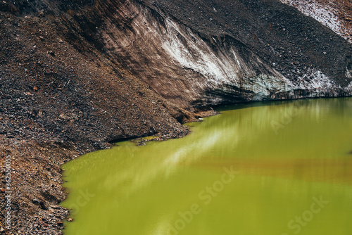 Stones on slope of glacier above mountain lake of acid green color. Beautiful emerald glacial lake and snowy slope of glacier with stones. Awesome alpine lake of unusual green tones. Amazing landscape