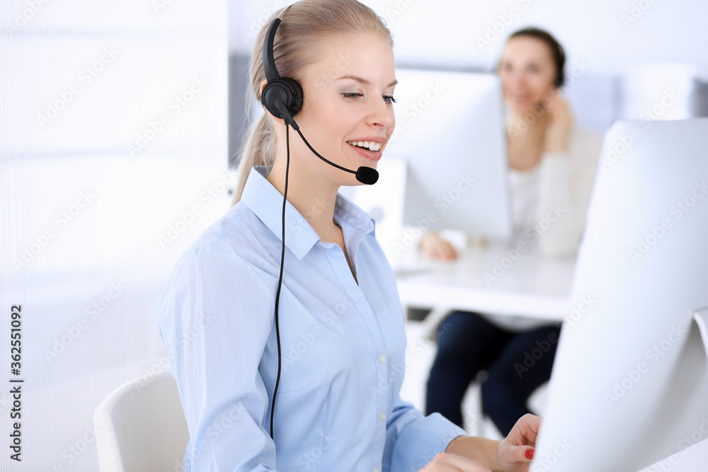Call center office. Beautiful blonde woman using computer and headset for consulting clients online. Group of operators working as customer service occupation. Business people concept Call center office. Beautiful blonde woman using computer and headset for consulting clients online. Group of operators working as customer service occupation. Business people concept
