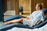 Beautiful woman in bathrobe relaxing on lounge chair at the spa.