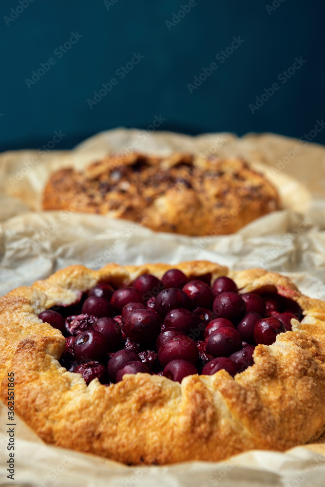 Two galettes with ripe red cherry and walnuts on dark background. Homemade sweet open pie. Two galettes with ripe red cherry and walnuts on dark background. Homemade sweet open pie.