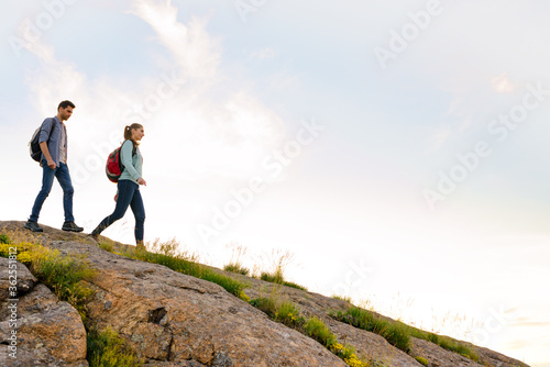 Couple of Young Happy Travelers Hiking with Backpacks on the Rocky Trail at the Evening. Family Travel and Adventure