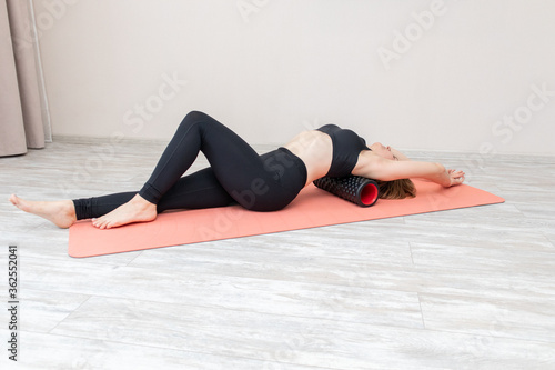 Sexy woman uses a foam roller massager for relaxation and doing yoga exercises