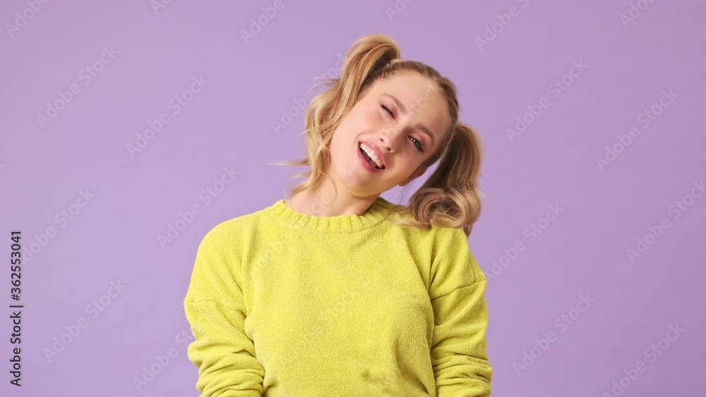 A fantastic girl in a yellow romantic sweater winks merrily and smiles at someone in the distance isolated in a studio on a purple background A fantastic girl in a yellow romantic sweater winks merrily and smiles at someone in the distance isolated in a studio on a purple background
