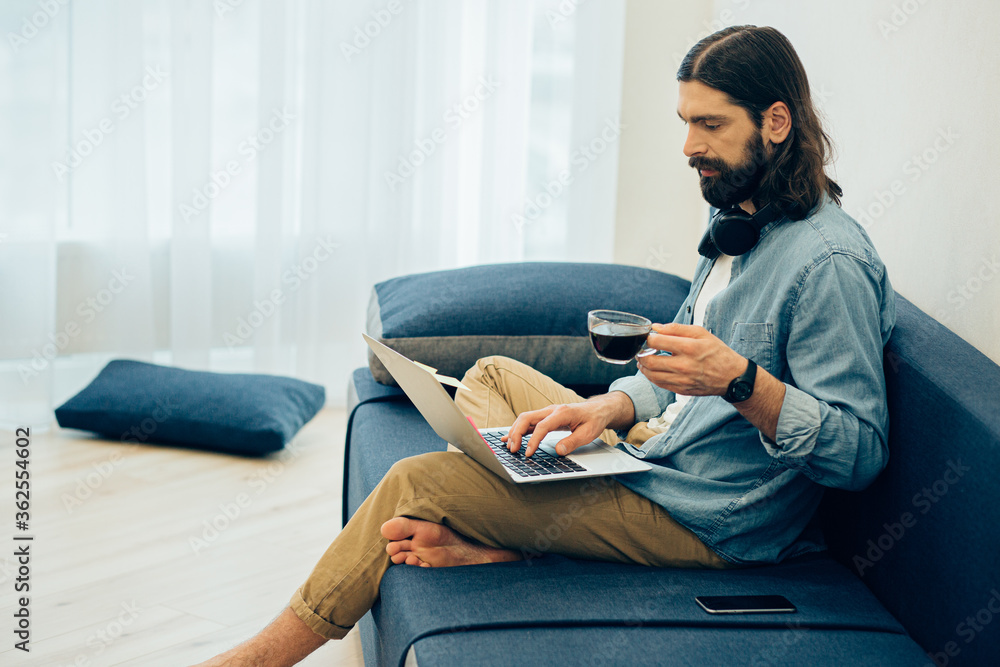 Calm man drinking coffee and working at home on the sofa Calm man drinking coffee and working at home on the sofa