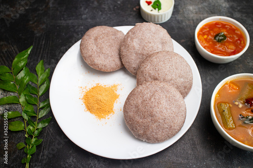 Ragi Idly, finger millet Idli, Sambar, coconut chutney healthy home made breakfast dish Kerala, Karnataka, India. steam cooked finger millet batter. Top view South Indian food dark black background. photo