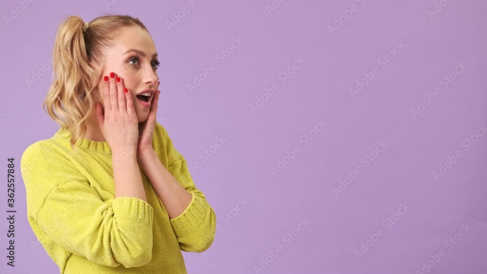 A delightful blonde girl in a yellow sweater crossed her arms then she saw something incredible, which she was very surprised and delighted in an isolated studio over a purple background A delightful blonde girl in a yellow sweater crossed her arms then she saw something incredible, which she was very surprised and delighted in an isolated studio over a purple background