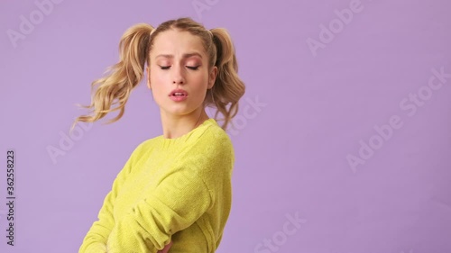 A cute blonde in a yellow sweater is unhappy and upset by the behavior of someone, sadly turned in the opposite direction, looking at the floor in an isolated studio on a purple background photo