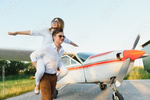 Happy young couple laughing and having fun on runway near private aircraft