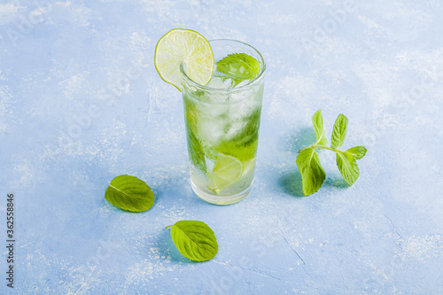 Refreshing cool detox drink with lime and mint on blue background. Summer lemonade or ice tea in a glass. Mojito cocktail with ice cubes. Healthy eating. Сopy space for text
