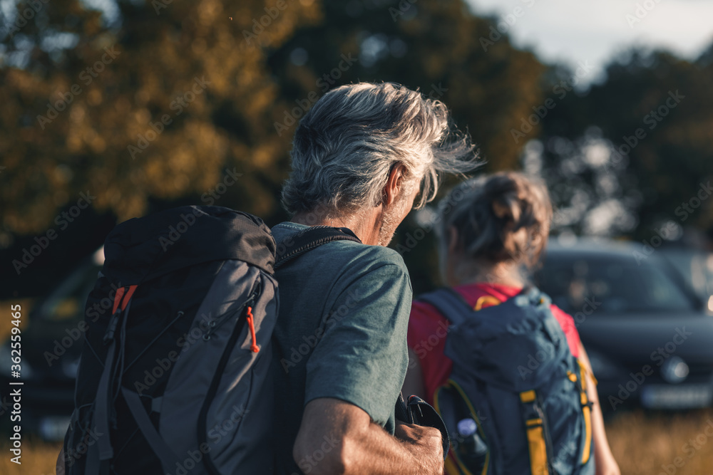 Fototapeta premium Active senior couple hiking in nature with backpacks, enjoying their adventure at sunset.