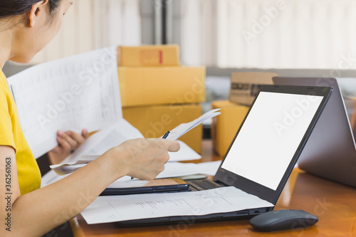 SME business online woman working on document with open laptop and parcel on table.