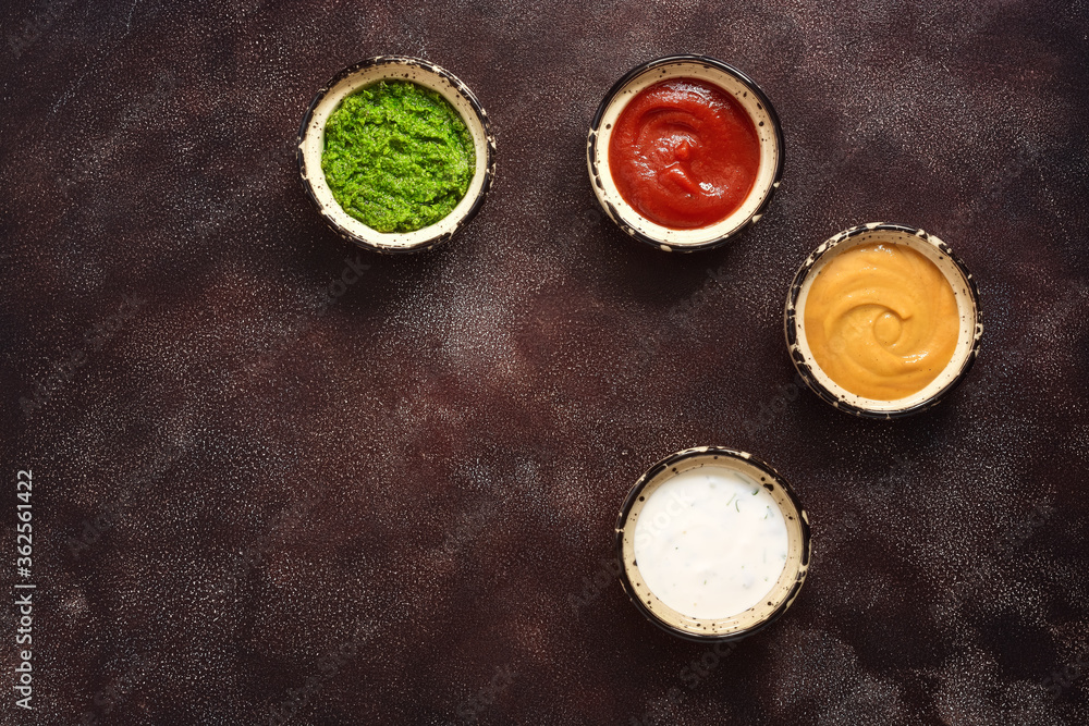 Collection of various sauces in the bowl: tomato, pesto, creamy with greens and mustard on a dark rustic background. Top view, copy space. Collection of various sauces in the bowl: tomato, pesto, creamy with greens and mustard on a dark rustic background. Top view, copy space.