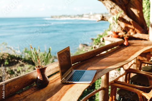 Fototapeta Naklejka Na Ścianę i Meble -  Open laptop with black screen  on wooden table work space outdoors with amazing view on the ocean. Laptop on sea view backdrop