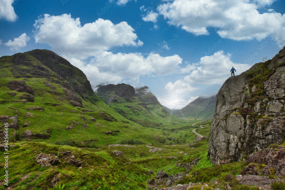 view into glencoe valley, highlands scotland with sunburst and person standing on rocks.