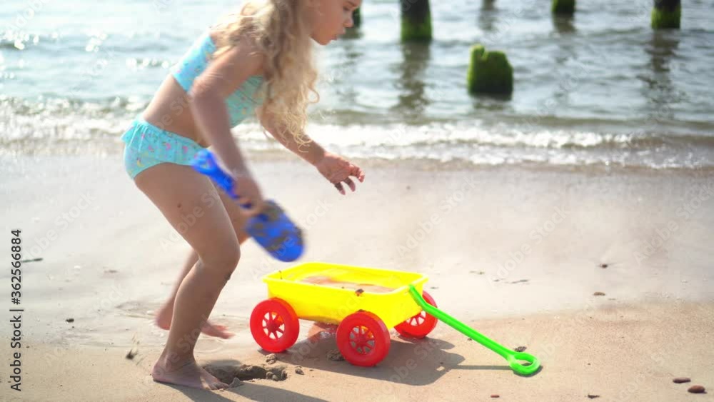 Little girl with curly blond hair playing with sand ant toy cart on sea shore Little girl with curly blond hair playing with sand ant toy cart on sea shore