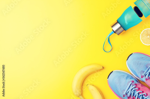 Fitness creative background - bottle with lemon water, fitness tracker, banana and snickers on yellow background, flat lay, copy space
