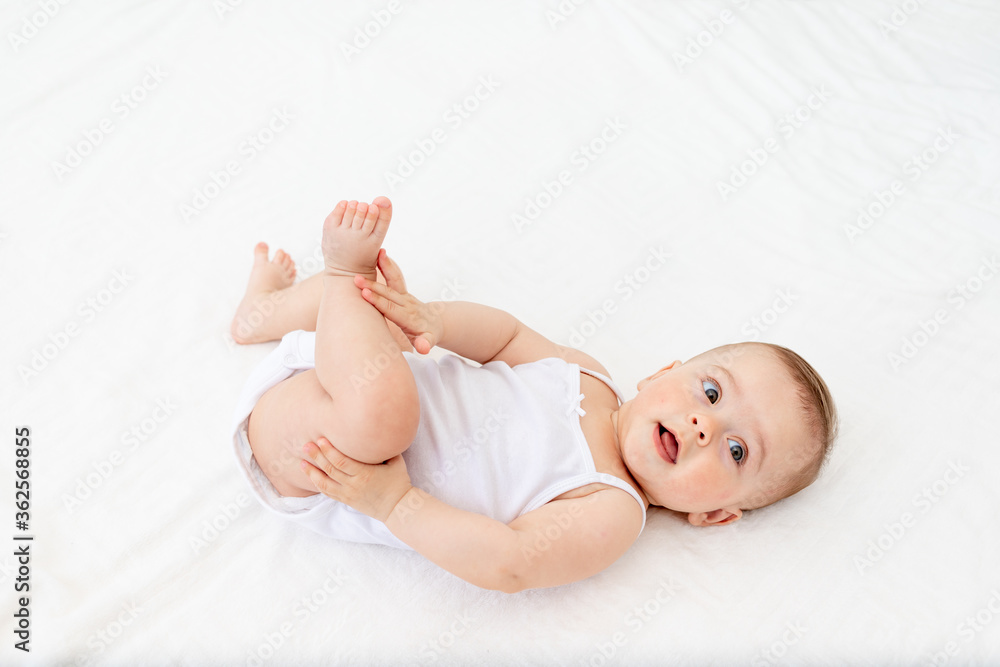 baby girl 6 months old lying in a crib in the children's room on her back and holding her legs, looking at the camera, baby's morning, baby products concept baby girl 6 months old lying in a crib in the children's room on her back and holding her legs, looking at the camera, baby's morning, baby products concept