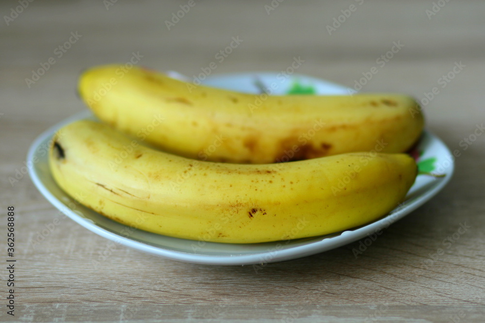 Two ripe yellow bananas lying in a beautiful white plate
