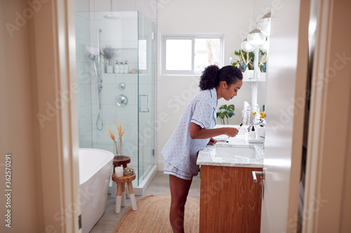 Woman Wearing Pyjamas Standing At Sink Brushing Teeth In Bathroom
