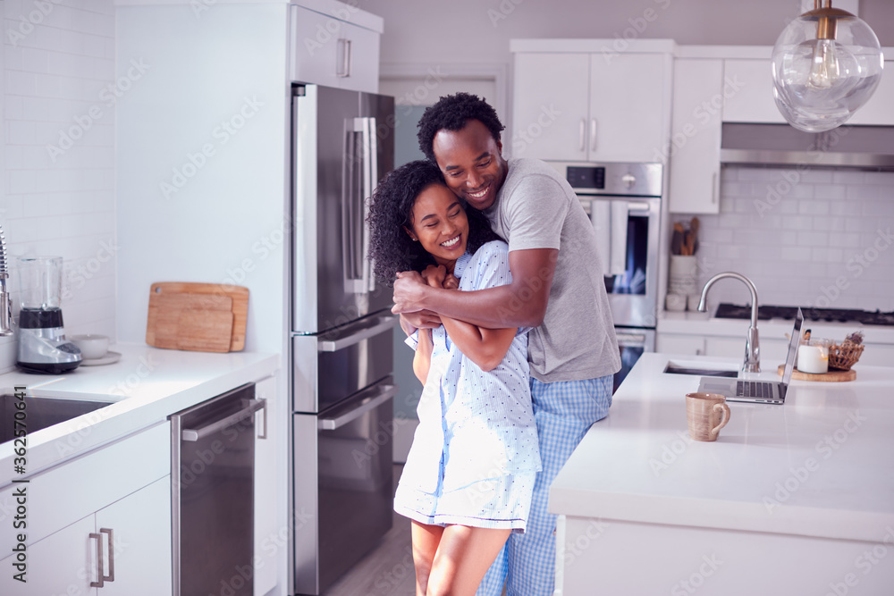Loving Couple Wearing Pyjamas Hugging In Kitchen At Home Together Loving Couple Wearing Pyjamas Hugging In Kitchen At Home Together