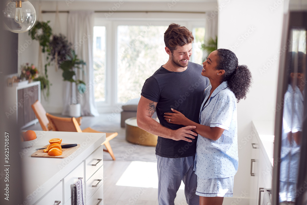 Loving Couple Wearing Pyjamas Hugging In Kitchen At Home Together Loving Couple Wearing Pyjamas Hugging In Kitchen At Home Together