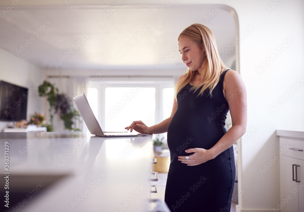 Pregnant Woman Standing By Kitchen Counter Working From Home On Laptop Pregnant Woman Standing By Kitchen Counter Working From Home On Laptop