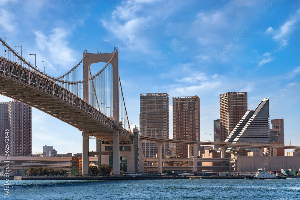 Double-layered expressway of the suspension Rainbow Bridge in the Tokyo Bay with a tugboat sailing in Tokyo port and the skyscrapers of the Shibaura-futō district in back