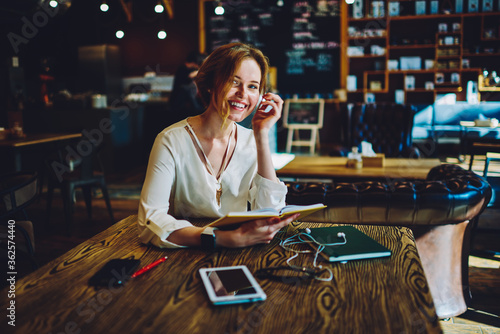 Portrait of cheerful female designer analyzing information from project plan having creative idea  charming businesswoman enjoying working process on successful startup sitting in coffee shop