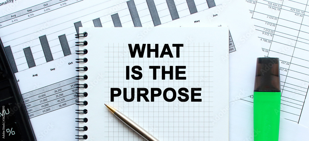 Text WHAT IS THE PURPOSE on the page of a notepad lying on financial charts on the office desk. Near the calculator and marker. Business concept. Text WHAT IS THE PURPOSE on the page of a notepad lying on financial charts on the office desk. Near the calculator and marker. Business concept.