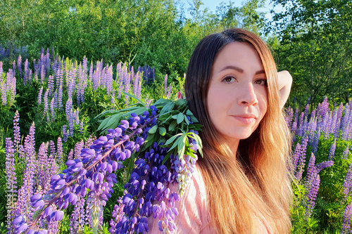 Close-up portrait of young caucasian woman with long red hair, against the background of greenery in  lupin`s field. Beautiful gathering flowers female.  photo