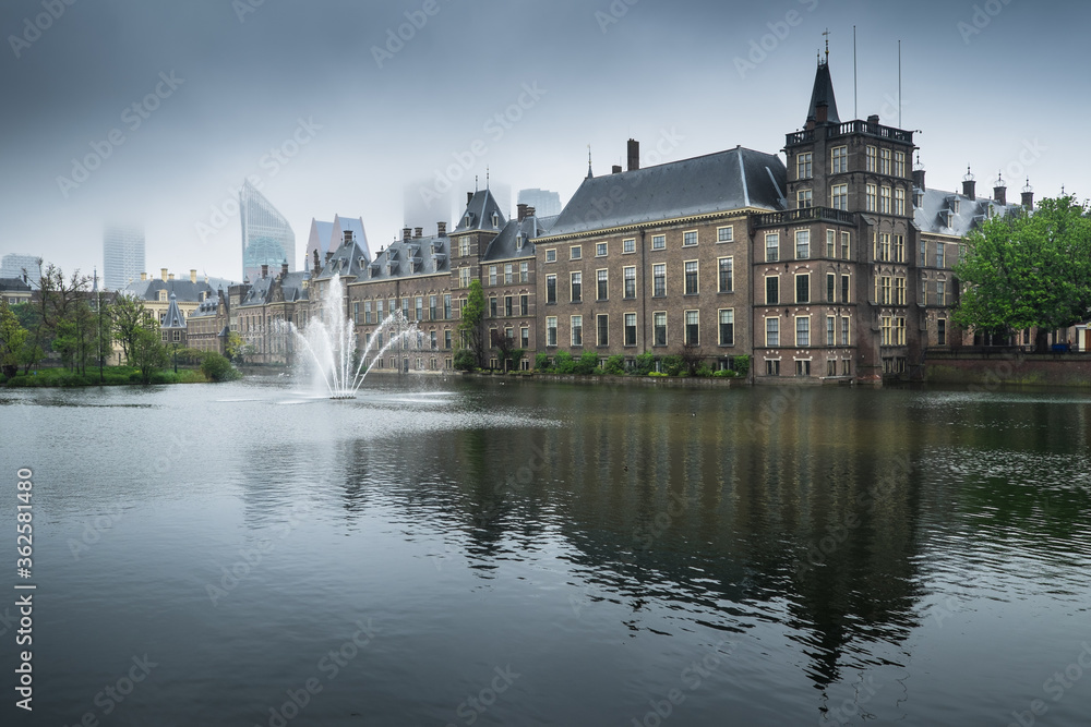 Binnenhof palace, place of Parliament in The Hague, Netherlands mirrored in the Hofvijver on a foggy day. Left the museum Mauritshuis