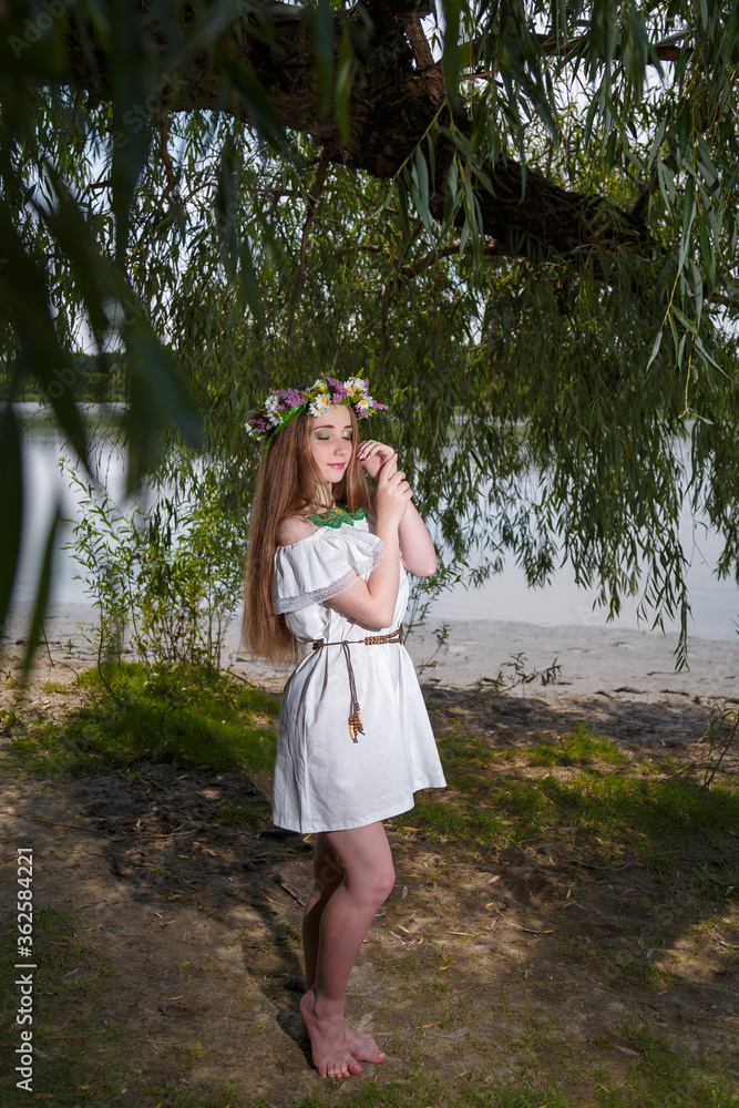 Beautiful girl in white dress and flowers wreath on green willow background. 7th July, traditional slavic holiday with fortune-telling and divination rituals in Ukraine. Beautiful girl in white dress and flowers wreath on green willow background. 7th July, traditional slavic holiday with fortune-telling and divination rituals in Ukraine.