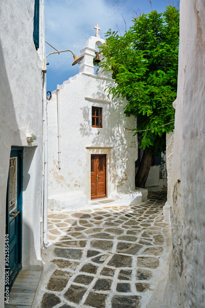 Picturesque scenic narrow Greek streets with traditional whitewashed houses with blue doors windows of Mykonos town and orthodox church in famous tourist attraction Mykonos island, Greece