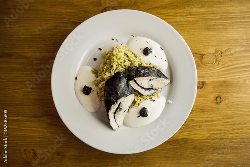 Close-up shot of boiled white rice and chicken fillet colored black with cuttlefish ink on plate.