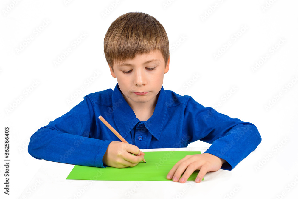 child development: a schoolboy boy in a blue T-shirt sits at the table and draws on colored paper child development: a schoolboy boy in a blue T-shirt sits at the table and draws on colored paper