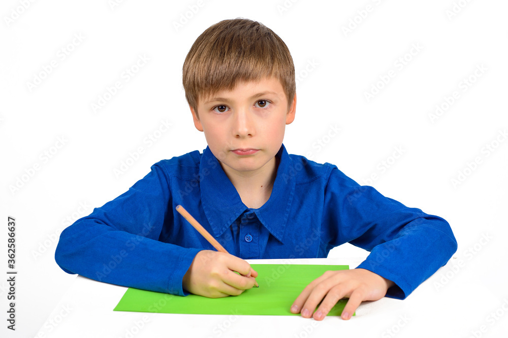 child development: a schoolboy boy in a blue T-shirt sits at the table and draws on colored paper child development: a schoolboy boy in a blue T-shirt sits at the table and draws on colored paper
