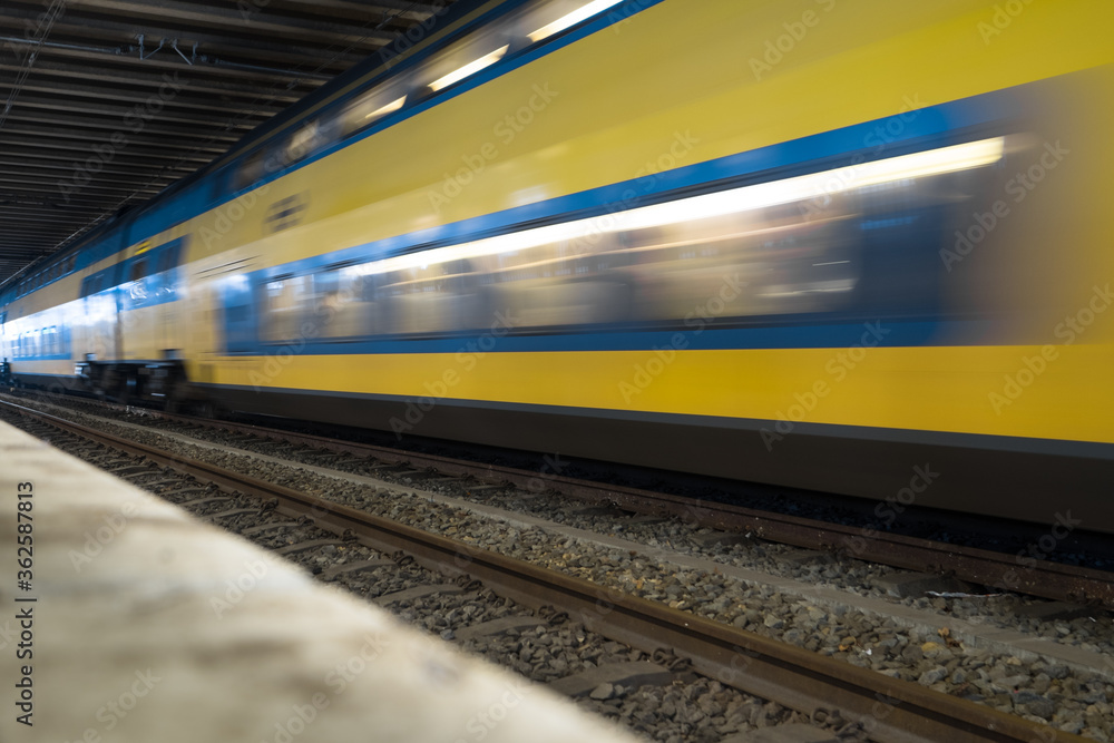 Dutch train with distinctive yellow and blue color passing by on a railway in train station in Rotterdam in the Netherlands