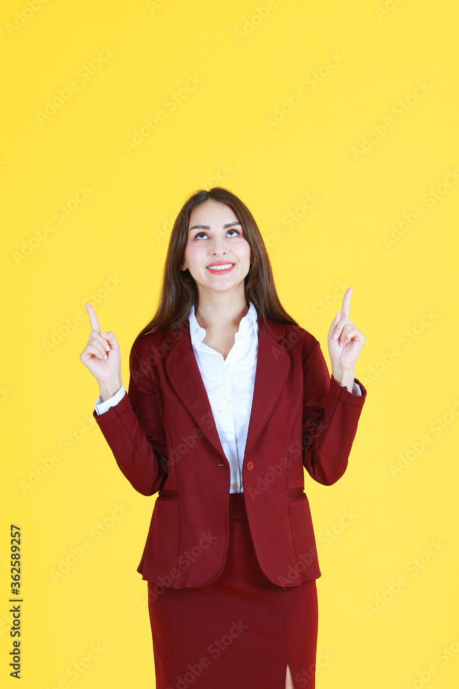Smart Caucasian woman in red suit smiling and her fingers Pointing top for present isolated on yellow background. Smart Caucasian woman in red suit smiling and her fingers Pointing top for present isolated on yellow background.