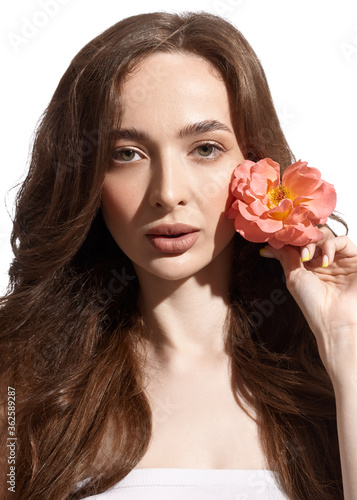 holding a rose flower in his hand. Young beautiful girl with fresh makeup and long hair. Spring look.
