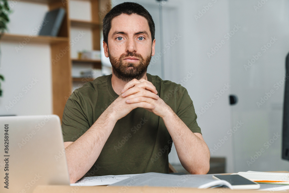 Fototapeta premium Photo of man looking at camera while working with laptop and drawings