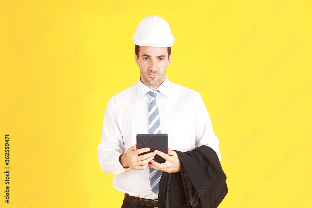 Handsome and smart engineer in suit and white shirt and Wearing a white safety engineer hat with hand holding smartphone isolated on yellow background. Copy Space Handsome and smart engineer in suit and white shirt and Wearing a white safety engineer hat with hand holding smartphone isolated on yellow background. Copy Space