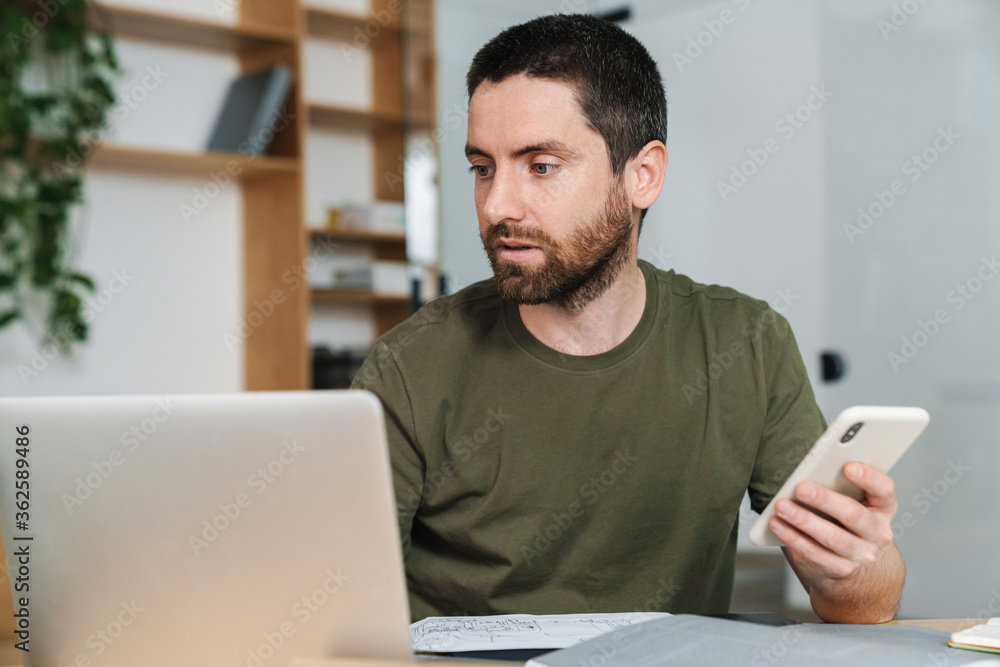 Photo of serious man working with laptop and cellphone Photo of serious man working with laptop and cellphone