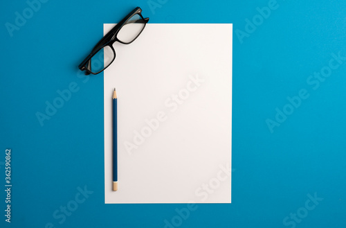 concept office white sheet, with black optical glasses, blue pencil, blue background.top view