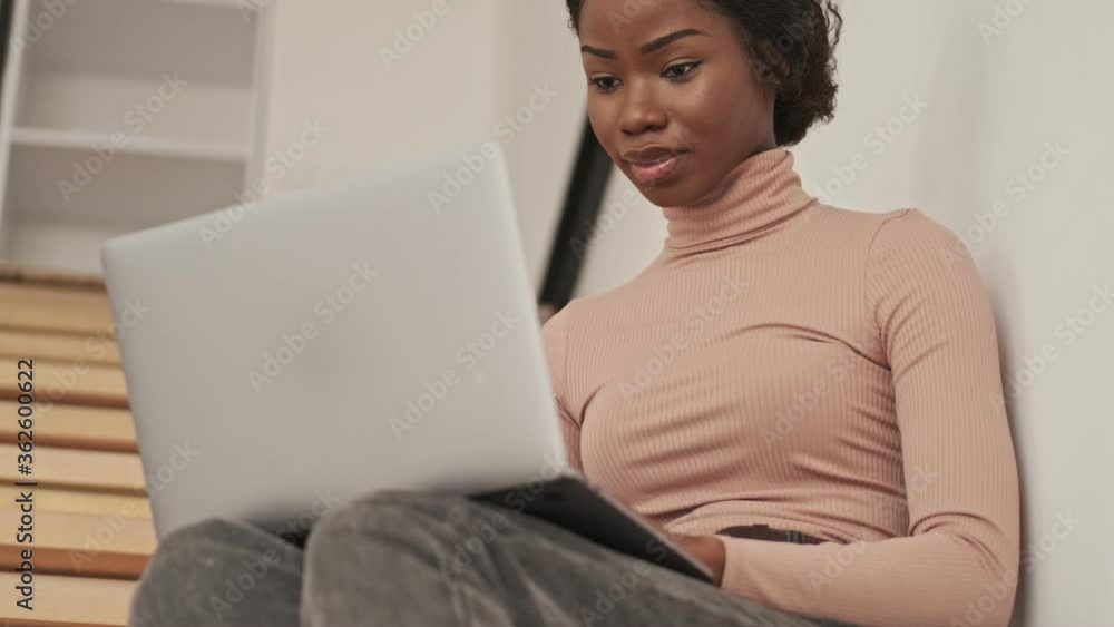A pretty pleased young african woman is using her laptop computer while sitting on a staircase at home A pretty pleased young african woman is using her laptop computer while sitting on a staircase at home