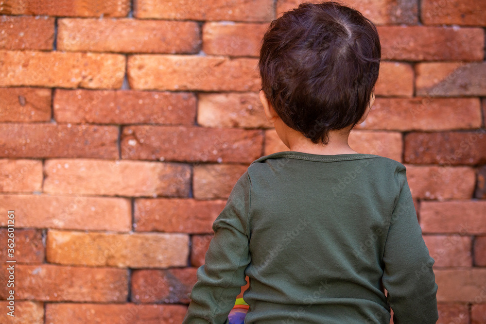 Small child standing facing a brick wall, bored and disobedient. Punishment.