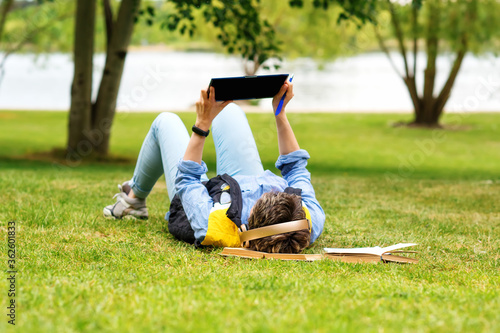 Woman lying on green grass and studying online on tablet